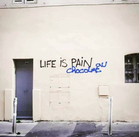 Graffiti on a house wall: Life is pain, with "au chocolat" added in blue